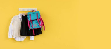 Sarı duvarda asılı okul üniforması ve sırt çantası. Tasarım için pankart