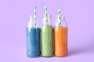 Cam şişeler, menekşe arkaplanda pipetle farklı lezzetli smoothie.