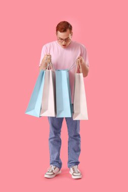 Pembe arka planda alışveriş torbalarıyla şok olmuş genç bir adam.