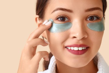 Bej arkaplanda göz altı bantları olan güzel genç bir kadın.