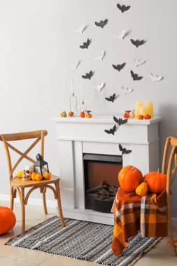 Cadılar Bayramı için dekore edilmiş oturma odasının içinde şömine, sandalye ve kağıt yarasalar var.