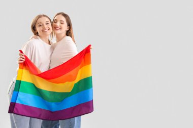 Açık arkaplanda LGBT bayrağı olan genç lezbiyen çift