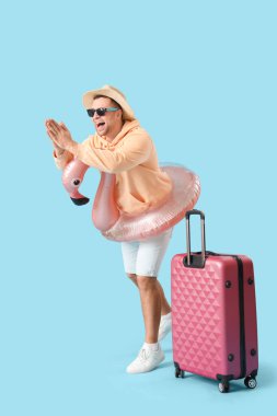 Bavullu ve şişme yüzüklü bir erkek turist mavi arka planda suya atlamaya hazırlanıyor.