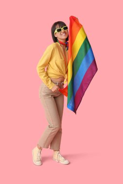 Pembe arka planda LGBT bayrağı olan güneş gözlüklü mutlu genç bir kadın.