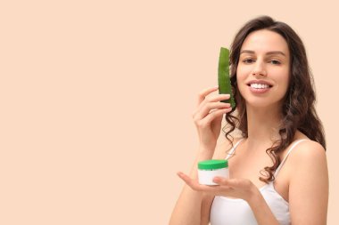 Aloe vera ve bej arka planda bir kavanoz kremayla güzel bir genç kadın.