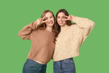 Mutlu gülümseyen genç kız kardeşler yeşil arka planda zafer jesti yapıyorlar.