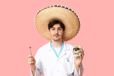 Fötr şapkalı genç erkek dişçi, pembe arka planda insan kafatası ve diş aynası çizmiş.