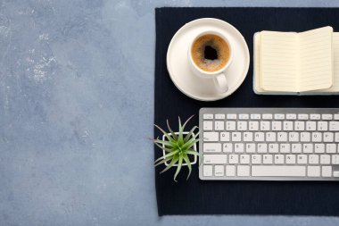 Mavi arka planda bir fincan kahve, çiçek ve defter olan modern bilgisayar klavyesi