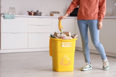 Mutfakta kağıt levhası olan çöpleri çöp kutusuna atan bir kadın. Geri dönüşüm kavramı