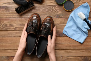 Hands with shoes, brushes, cloth and shoe polish on wooden background