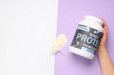 Bir şişe protein tozu ve renkli arka planda kepçeyle kadın eli.