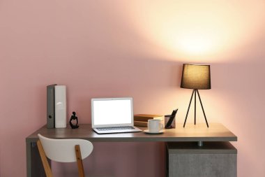 Modern dizüstü bilgisayarı ve pembe duvarın yanında parlayan lambası olan rahat bir iş yeri.