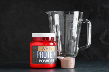 Koyu arkaplanda bir şişe protein tozu ve blender.