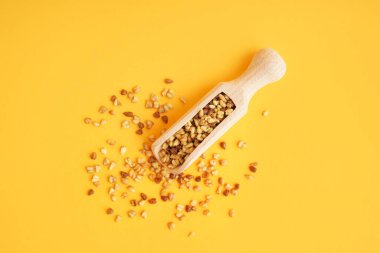 Turuncu arka planda çiğ karabuğday taneleri olan ahşap kepçe.