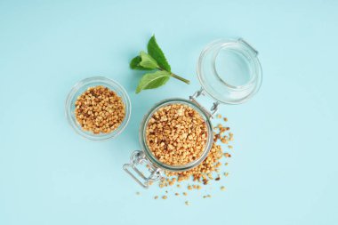 Ham karabuğday taneli cam kavanoz ve mavi zemin üzerinde nane.