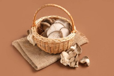 Kahverengi arka planda taze istiridye mantarlı hasır sepeti.