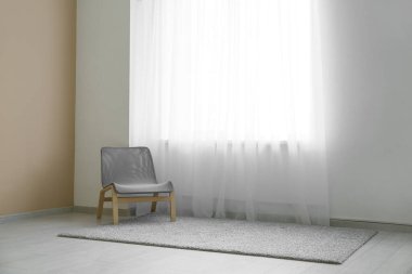 Odadaki ışık perdesinin yanındaki sandalye ve halı.