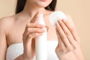 Pamuklu pedi olan genç bir kadın ve bej arka plandaki makyajı silmek için deniz suyu, yakın plan.