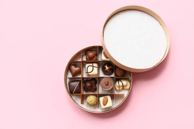 Pembe arka planda lezzetli çikolata şekerleriyle dolu bir kutu.