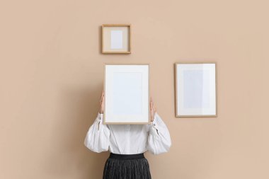 Şık bir odada bej duvarın yanında resim çerçevesi tutan genç bir kadın.