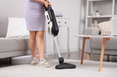 Young woman cleaning carpet with cordless stick vacuum cleaner in living room