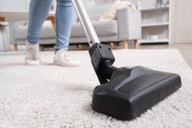 Young woman cleaning carpet with cordless stick vacuum cleaner in living room, closeup