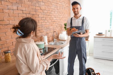 Erkek teknisyen ve kadın mutfakta kırık fırının yanında.