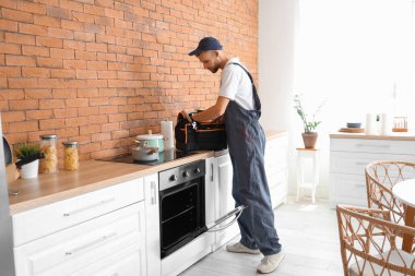Mutfakta fırını tamir eden alet çantalı bir erkek teknisyen.