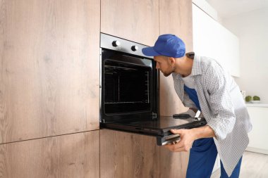 Erkek teknisyen mutfakta elektrikli fırını kontrol ediyor.