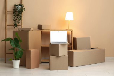 Boş dizüstü bilgisayar, taşınan kutular, parlayan lamba ve odada bej duvarın yanındaki bitkiler.