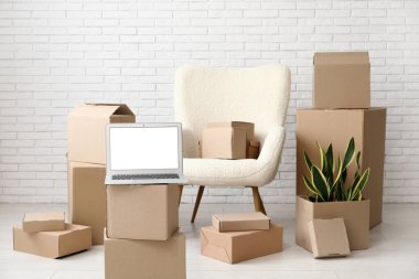 Boş dizüstü bilgisayar, taşınan kutular ve beyaz tuğla duvarın yanındaki koltuk.