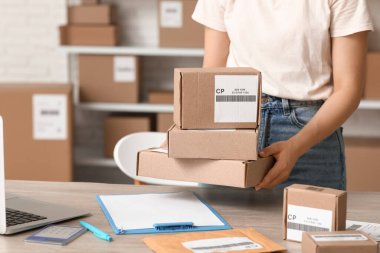 Kadın postacı, paket kutularını masaya koyar, yakın plan.