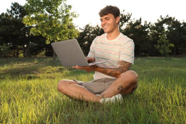 Dışarıda çimlerin üzerinde dizüstü bilgisayarı olan genç adam.