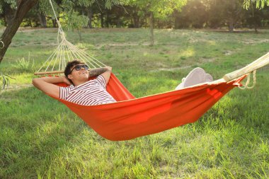 Dışarıda hamakta dinlenen güneş gözlüklü genç adam.