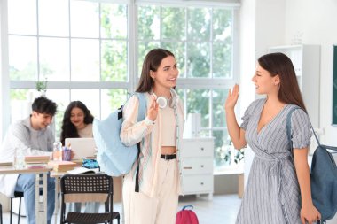 Sırt çantalı genç kız öğrenciler sınıfta el sallıyor.