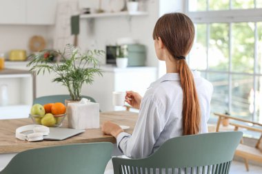 Bir fincan kahveli genç kadın yemek odasında, arka planda oturuyor.