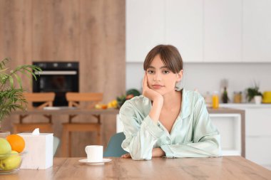 Yemek odasındaki masada bir fincan kahveyle oturan genç kadın.