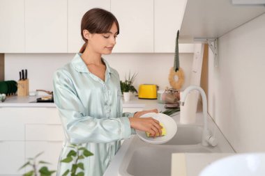 Genç bir kadın mutfakta bulaşık yıkıyor.