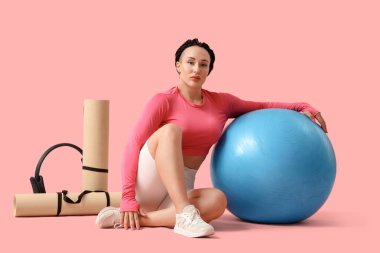 Pembe arka planda oturan spor aletleri olan kadın vücut geliştirici.