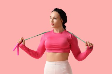 Pembe arka planda ip atlayan kadın vücut geliştirici.