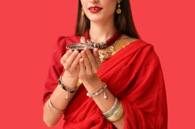 Kırmızı arka planda diya lambası olan sarili güzel Hintli kadın, yakın plan.