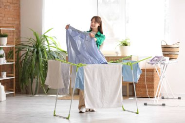 Çamaşır odasında kurutma makinesinin yanında temiz gömlekli genç bir kadın.