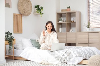 Bilgisayarlı genç Asyalı kadın yatak odasında online randevusu var.