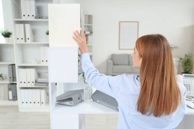 İş kadını ofisteki raftan doküman klasörünü alıyor.