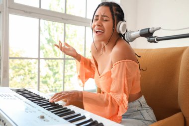 Mikrofonlu ve sentezleyicili genç Afro-Amerikalı kadın stüdyoda şarkı söylüyor.