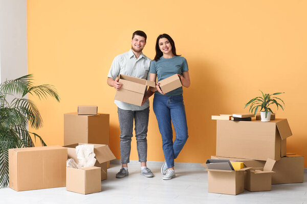 Young happy couple with belongings near orange wall in their new house