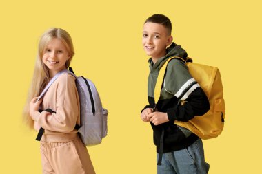 Sarı arka planda sırt çantaları olan sevimli öğrenciler.