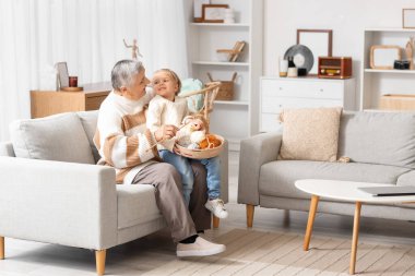 Şirin küçük kız ve örgü ören büyükannesi evdeki kanepede oturuyor.