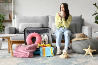 Güzel genç bayan oturma odasının içinde bavul hazırlarken hindistan cevizi içiyor.