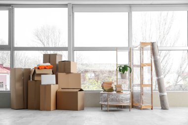 Taşındığı gün şık bir odada cam kenarında rulo halı, sehpa ve karton kutular.